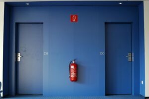 Blue doors in a corridor with a red fire extinguisher between them.
