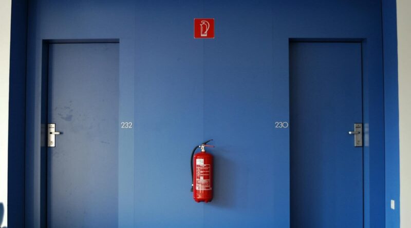 Blue doors in a corridor with a red fire extinguisher between them.